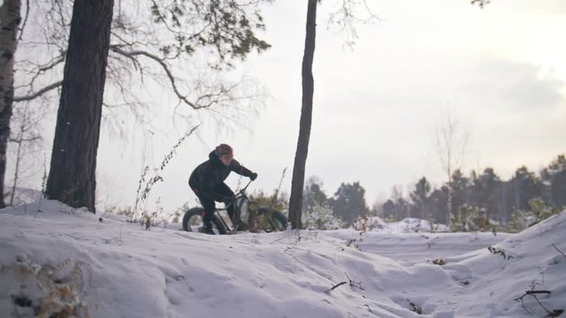 Professional extreme sportsman biker riding fat bike in outdoors. Cyclist ride in winter snow forest. Man does trial trick bunny hop jump on mountain bicycle with big tire in helmet and glasses.