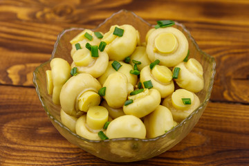 Glass bowl with pickled champignons. Marinated mushrooms on wooden table