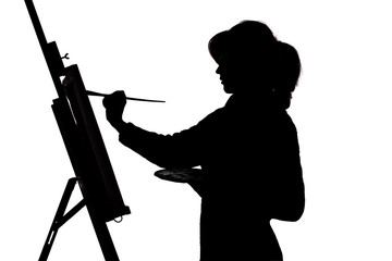 silhouette of a young woman painting on an easel on a white isolated background, the figure of a...