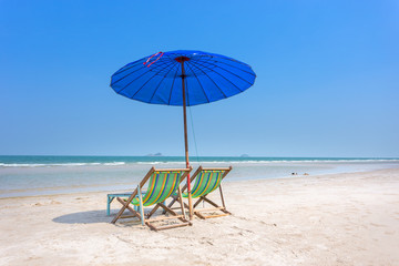 wood beach chair with blue umbrella on white sand beach with sea in summer