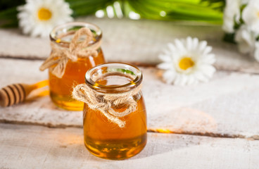 Obraz na płótnie Canvas Glass jar of honey with wooden drizzler and chamomile