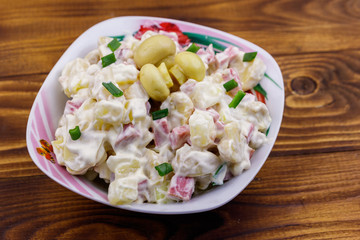 Potato salad with marinated mushrooms, sausage, onion and mayonnaise on wooden table