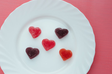 Heart shaped marmalade on a white plate pink background close-up. Valentine's day concept.