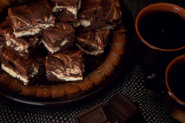 Dessert. Chocolate and curd brownie. The cake is stacked in several rows on a dark plate. Shot in a rustic style in a low key.