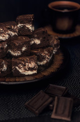 Dessert. Chocolate and curd brownie. The cake is stacked in several rows on a dark plate. Shot in a rustic style in a low key.