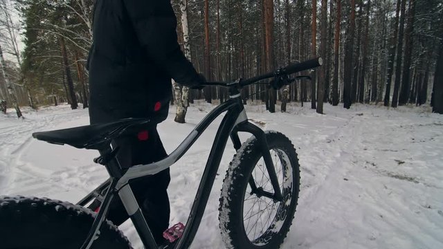 Professional extreme sportsman biker walk with fat bike in outdoors. Cyclist walking in the winter snow forest. Man go on mountain bicycle with big tire in helmet and glasses. Slow motion in 180fps.