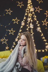 young woman in a plaid posing against the background of Christmas garlands.