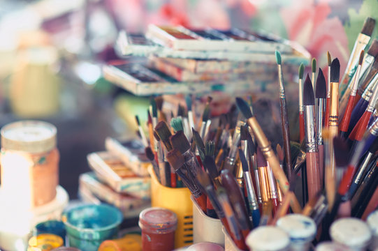 Paint brushes and watercolor paints on the table in a workshop, selective focus, close up.