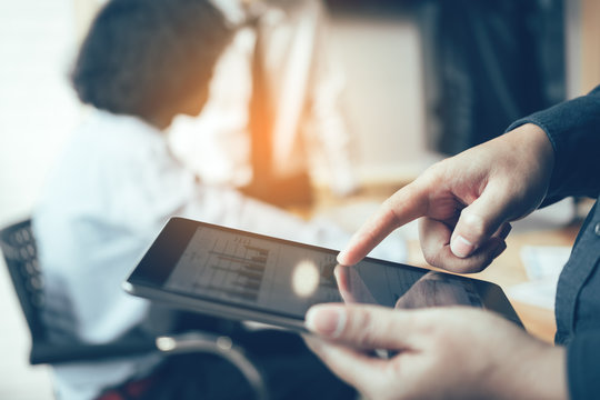Business people examining financial reports and analyzing business growth on tablet in boardroom.