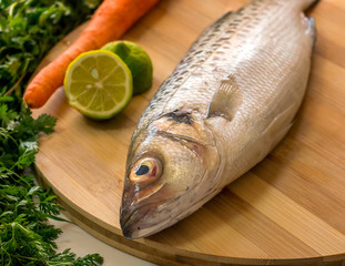 Fresh Raw Sea Bass Fish On a Cutting Board with Vegetables