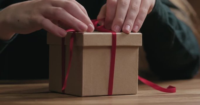 Closeup shot of young female hands opens craft paper gift box with red ribbon bow
