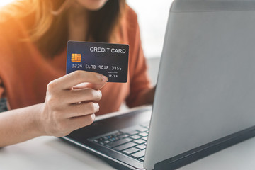 Young asian woman holding mockup credit card and use laptop for purchase product on internet in home office, Cyber Monday shopping online concept, Copy space.