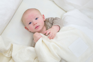 Baby boy in white sunny bedroom. Newborn child relaxing in white bed. Nursery for children. Textile and bedding from bio cotton for kids. New born kid with bio cotton blanket.