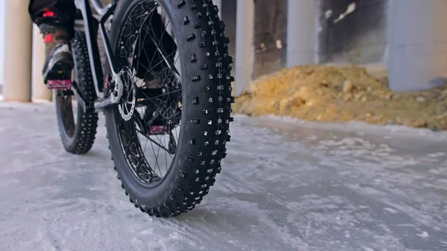 Professional extreme sportsman biker riding fat bike in outdoors. Close-up view of rear wheel. Cyclist ride in winter forest. Man on mountain bicycle with big tire. Snow fly into the lens camera.
