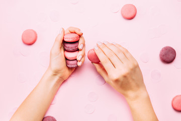 Obraz na płótnie Canvas Beautiful female hands with trendy manicure holding pink macaroon cake. Top view, flat lay. Copyspace for your text.