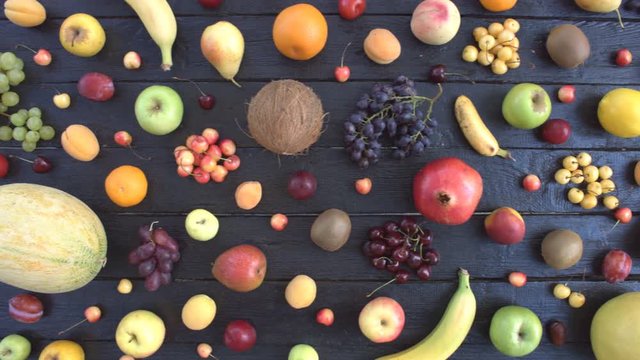 Fruits on black ecological background. Top view. Various fruits are located on black wooden eco background. On eco table are: coconat, grapes, oranges, bananas, cherries, lemon, tangerines.