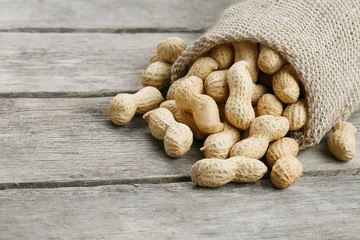 Peanuts in a miniature burlap bag on old, gray wooden surface
