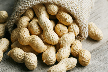 Peanuts in a miniature burlap bag on old, gray wooden surface