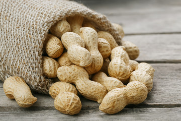 Peanuts in a miniature burlap bag on old, gray wooden surface