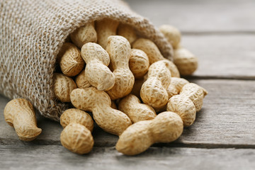 Peanuts in a miniature burlap bag on old, gray wooden surface