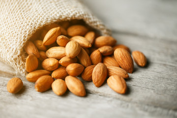 Almond nuts in a burlap bag on a wooden gray background.