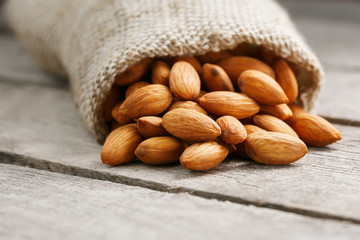 Almond nuts in a burlap bag on a wooden gray background.