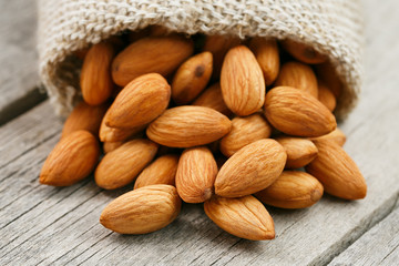Almond nuts in a burlap bag on a wooden gray background.