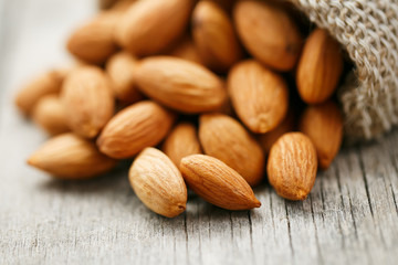 Almond nuts in a burlap bag on a wooden gray background.