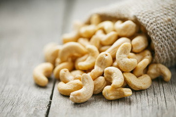 Cashew nuts in burlap bag on wooden gray background . Healthy food