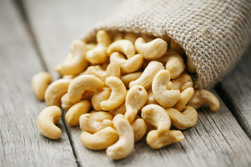 Cashew nuts in burlap bag on wooden gray background . Healthy food