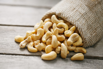 Cashew nuts in burlap bag on wooden gray background . Healthy food