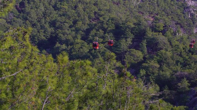 Cableway on picturesque mountains. Red cabins driving over huge green trees growing on rocks. Real time 4k video footage.