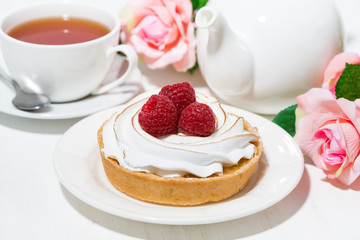 sweet tartlet with meringue and raspberry, cup of tea on white table
