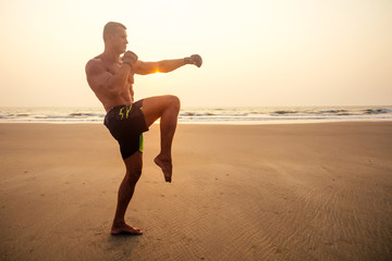 Fototapeta na wymiar Muscular and fit young bodybuilder man doing workout warm up stretching on a paradise beach at sunset.fitness male model sport on sea