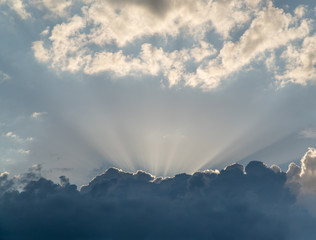 Obraz na płótnie Canvas Sun rays from behind clouds on blue sky