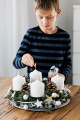 Young boy lighting the first candle on Advent Wreath on the first Sunday in December. Celebrating...