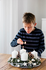 Young boy lighting the first candle on Advent Wreath on the first Sunday in December. Celebrating Christmas holidays, swiss tradition.