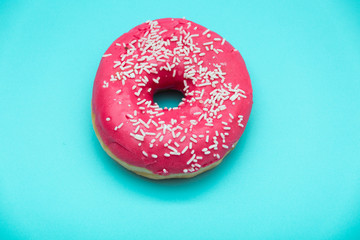 Pink donut with colorful sprinkles isolated on blue background. Top view.