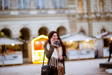 Obraz premium Smiling young woman using phone on street at cold winter day