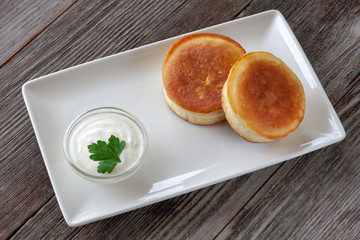 Vegetarian breakfast: thick pancakes with sour cream on a white rectangular plate