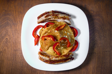 fried sausages pancakes and red pepper lie on a white plate.