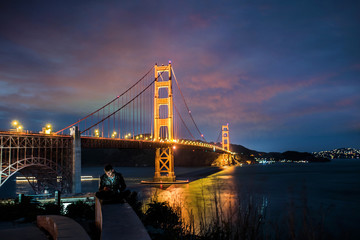 Obraz na płótnie Canvas jeune homme regardant son portable au pied du Golden Gate Bridge
