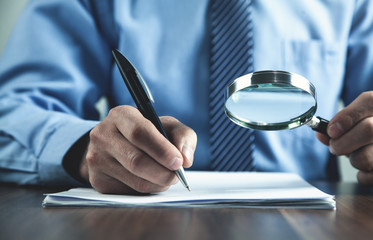 Man writing on document and using magnifying glass.