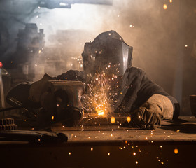 Welder is welding metal part in factory