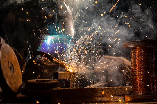 Welder is welding metal part in factory