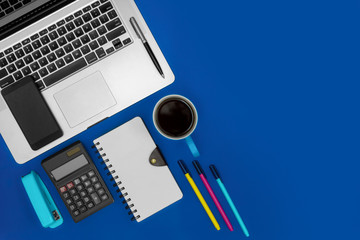 Office desk working space. Laptop, notebook, calculator and coffee on blue background. Business concept.