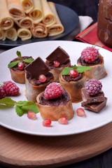 Rolled crepes with chocolate paste topped with raspberries, pomegranate, mint and chocolate pieces on a white plate