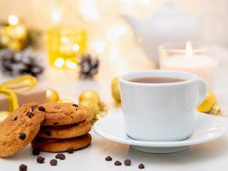 Chocolate chip cookies, cup of tea on light christmas background. Cozy evening, mug of drink, Christmas decorations, candles and lights garlands
