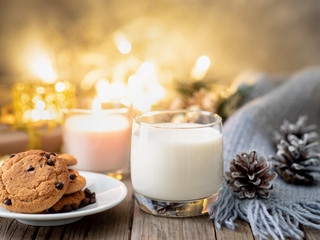 Christmas background with chocolate chip cookies, glass of milk. Cozy evening, mug of drink, dark Christmas decorations, candles and lights garlands