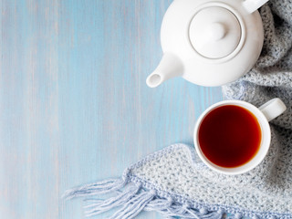 tea, teapot, copy space, warm knitted scarf on blue wooden background, cozy house, top view